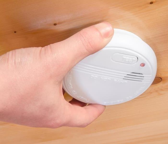 Hand installing white ceiling home smoke detector alarm