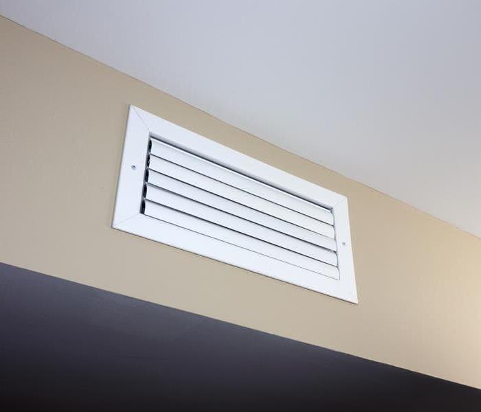 A white rectangle air vent from a duct of an indoor HVAC system in a beige color wall near a ceiling
