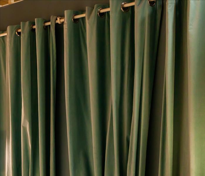 Deep green drapes on a brass curtain rod hanging on a dark painted wall